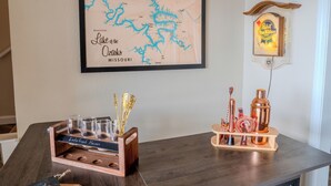 Une carte encadrée du lac des Ozarks, dans le Missouri, un plateau en bois avec des verres et un chandelier, et une horloge au mur.