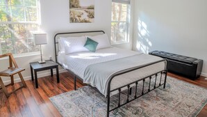 Une chambre à coucher comprenant un lit, une table de chevet, une chaise, un banc et deux fenêtres.