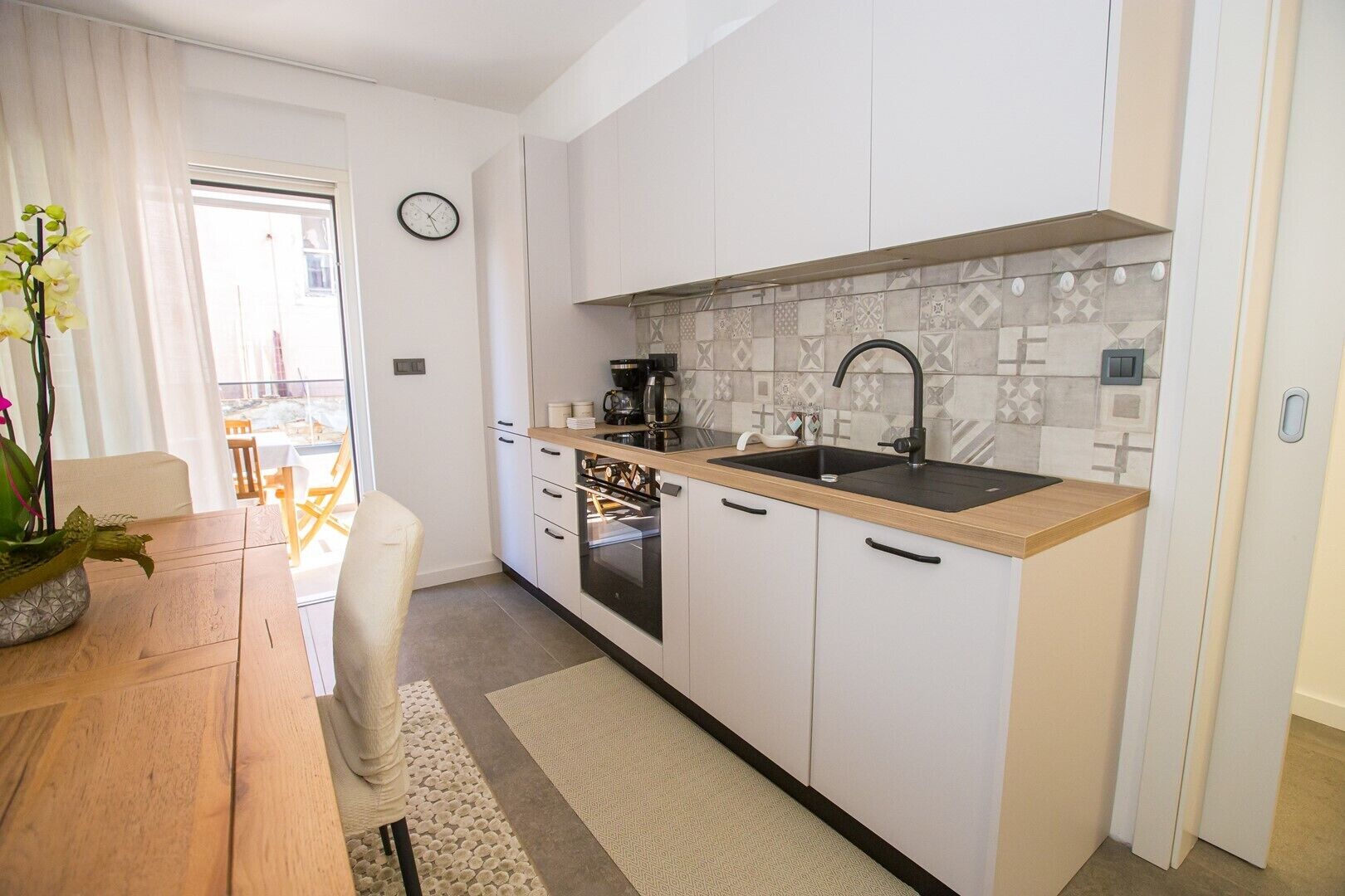 A modern kitchen with white cabinets, a wooden countertop, a black sink, and a patterned backsplash.