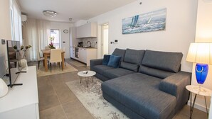 A modern living room with a grey sofa, a small round coffee table, and a dining area with a white table and chairs. - Apartman Sonia in Porec (Porec)