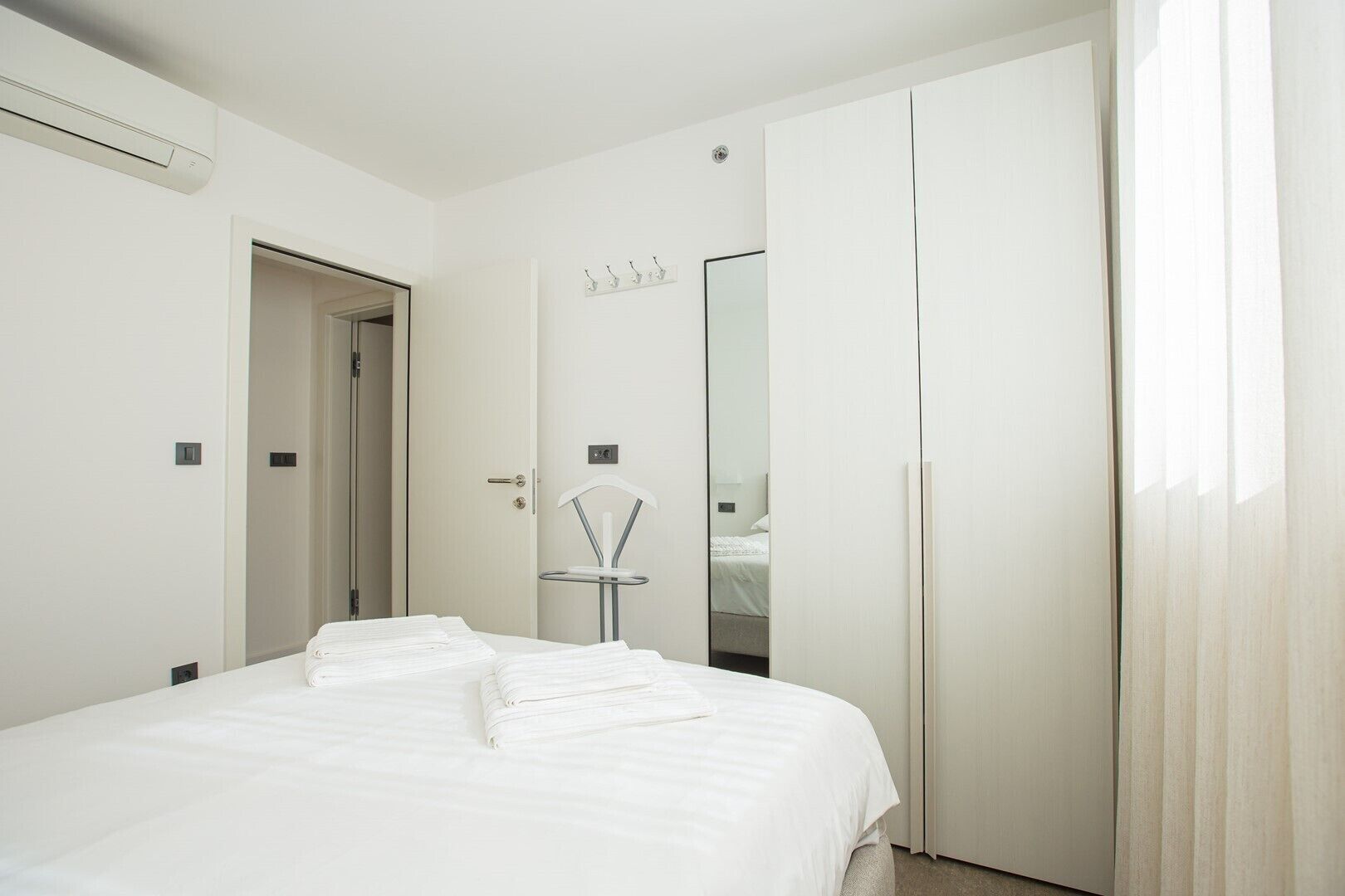 A hotel room with a bed, a wardrobe, a mirror, and a hanging towel rack.