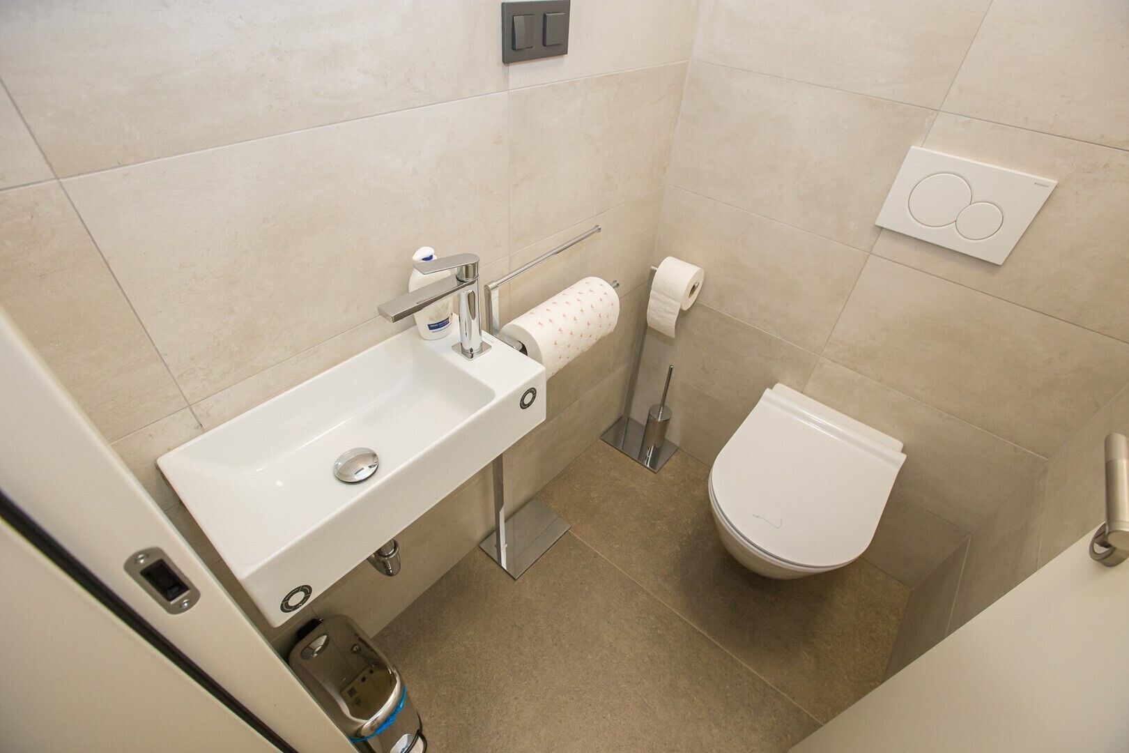 A modern bathroom with a white sink, toilet, and a towel dispenser.