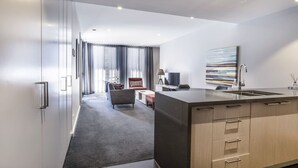 Habitación de hotel moderna con cocina central grande, zona de estar con sofá y sillón, y vista a la ciudad.