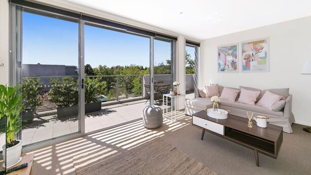 Een moderne woonkamer met een grote schuifpui naar een balkon, een bank, een salontafel en een televisie.