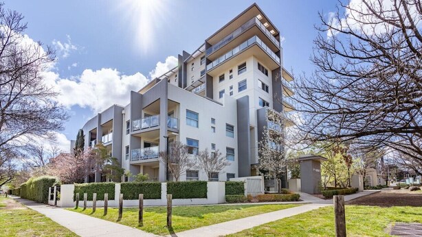 Een modern appartementencomplex met meerdere verdiepingen, balkons, een verzorgd gazon en een heldere lucht.