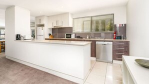 Een moderne keuken met witte kasten, een centraal eiland, roestvrijstalen apparatuur en een raam met zonwering.