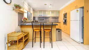 A modern kitchen with a central island, wooden cabinets, a refrigerator, and a clock on the wall.