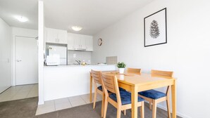 Une cuisine moderne avec des meubles blancs, un four encastré et un coin repas comprenant une table et des chaises en bois.
