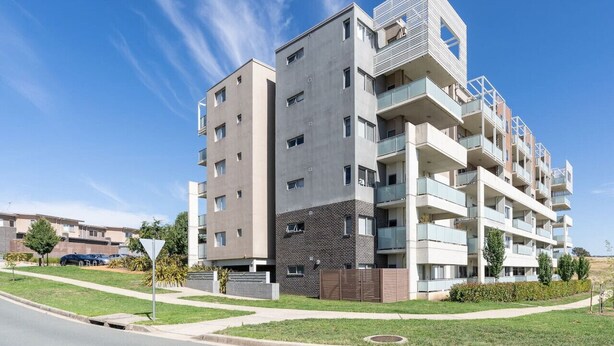 Un immeuble d’appartements moderne à plusieurs étages, doté de balcons, d’un espace de stationnement et surplombant un ciel dégagé.
