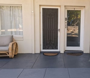 A building entrance with a metal gate, a number '8' on the door, a wicker chair outside, and a doormat.