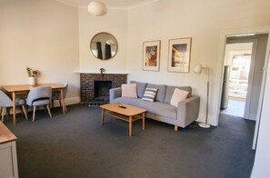 A living room with a sofa, coffee table, and a fireplace. There is a dining area with a table and chairs.