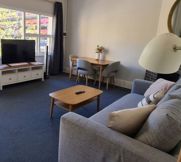 A living room with a sofa, a coffee table, a TV on a stand, a dining table with chairs, and a lamp.