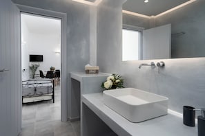 A modern bathroom with a large white sink, a mirror, and a shower area.