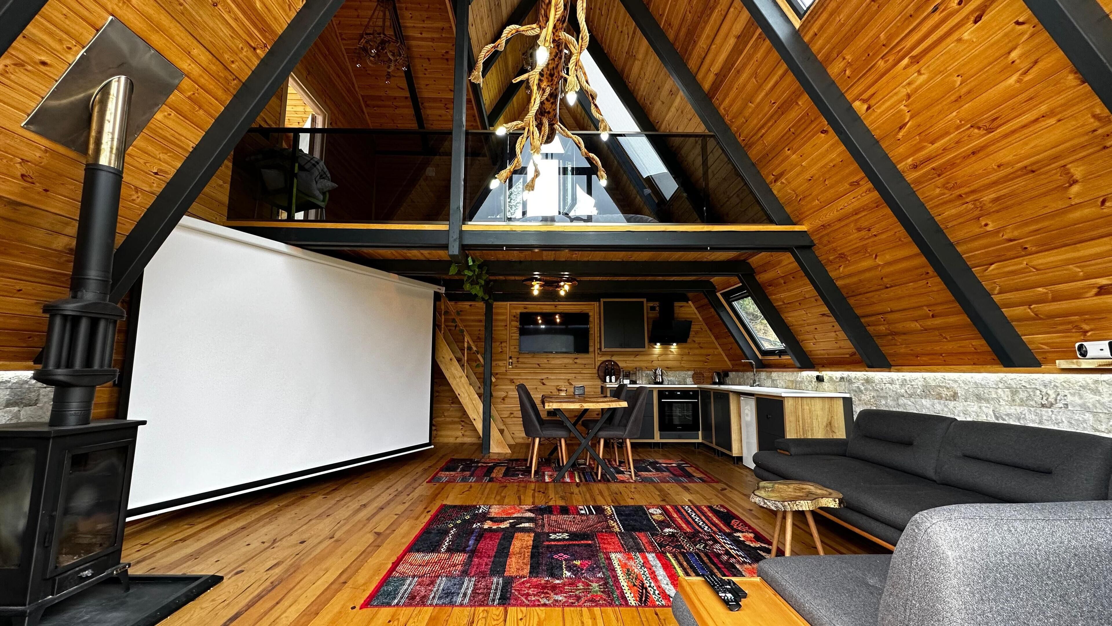 Acogedor dormitorio en el ático, con techo de madera, chimenea, zona de comedor y sofá.