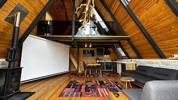 Acogedor dormitorio en el ático, con techo de madera, chimenea, zona de comedor y sofá.