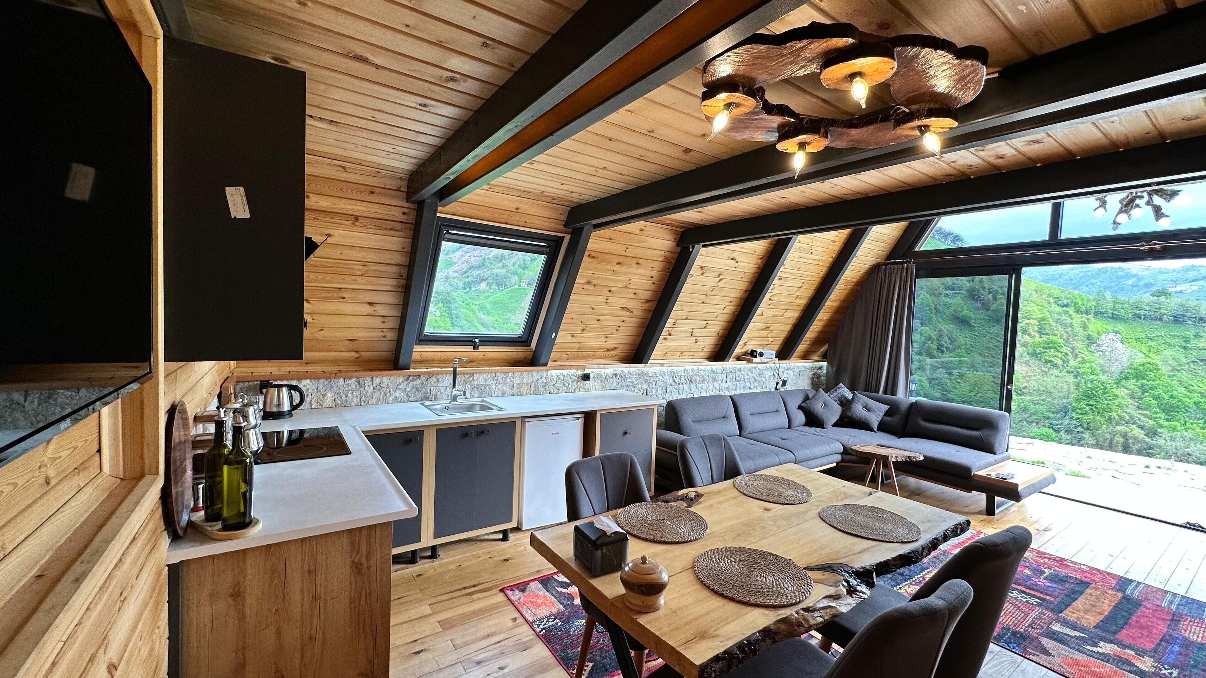 Una cocina moderna con comedor, vigas de madera en el techo y grandes ventanales con vistas al exterior.
