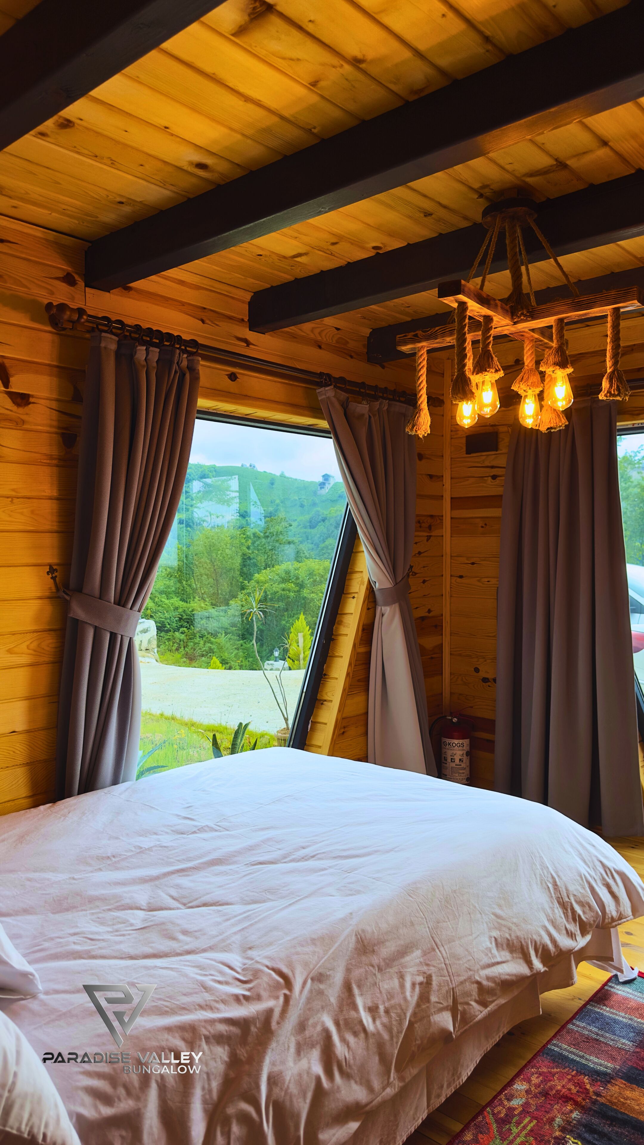 Een slaapkamer met een groot bed, houten balken in het plafond en uitzicht op groen.