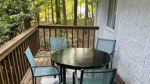 Une terrasse en bois avec une table ronde et quatre chaises, entourée d’une rambarde et d’un tapis à motifs.