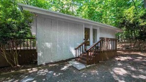 Une petite cabane à un seul étage, avec un escalier en bois menant à une porte, le tout entouré d’arbres.