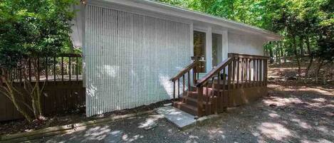 A small, single-story cabin with a wooden staircase leading to a door, surrounded by trees.