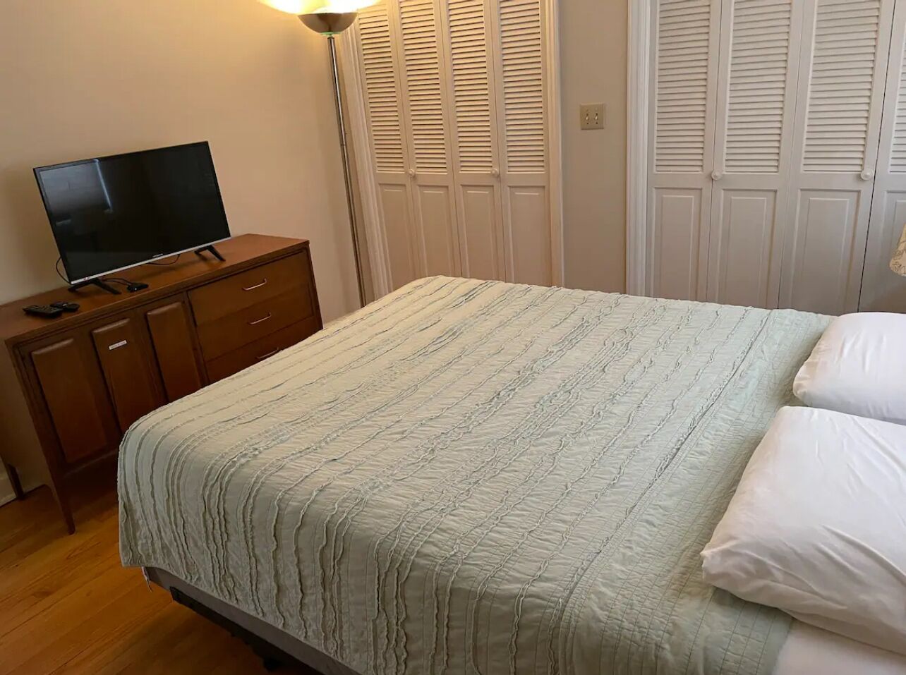 A bedroom with a bed, a TV on a wooden dresser, and white closet doors.