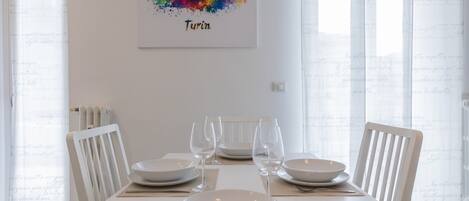 A dining area with a white table set for four, a framed cityscape artwork above, and a radiator on the wall.