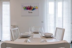 A dining area with a white table set for four, a framed cityscape artwork above, and a radiator on the wall. - Casa Gabri by Wonderful Italy (Turin)