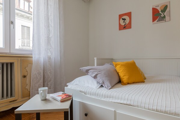 Un dormitorio con una cama individual, una mesita de noche con un libro y una taza, y dos obras de arte en la pared.