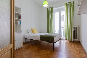 Un dormitorio con cama, mesita de noche, estantería y ventana con cortinas.