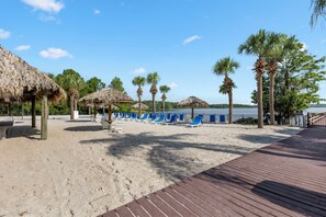 A beach with thatched-roof structures, palm trees, and a wooden boardwalk leading to the water. - Family Fun Awaits! 10% OFF 7Night Stay Resort Access + Patio & 15min to Disney (Davenport)