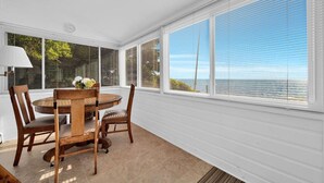 A dining area with a round table and chairs, large windows with blinds, and a view of the ocean. - Lakefront 3BD, Home Walk to Downtown Port Sanilac (Port Sanilac)