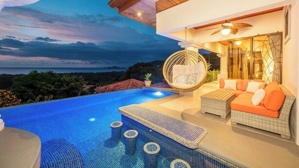 A modern outdoor pool area with a hanging chair, a sofa, and a ceiling fan. - Casa del Mar • 4 BR Ocean-View Villa with Private Pool & BBQ • 8 Guests (Playa Hermosa)