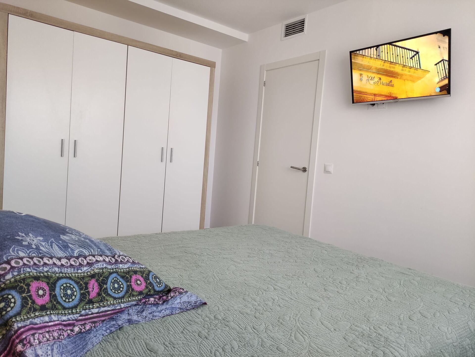 Un dormitorio con cama, televisión en la pared y armario.