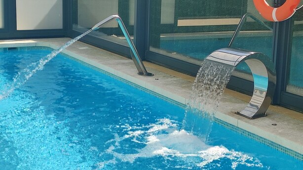 A swimming pool with a water feature, a lifebuoy, and a glass enclosure. - COVACHOS BEACH APARTMENT (Soto de la Marina)