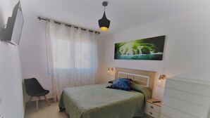 A bedroom with a bed, a chair, a nightstand, a dresser, a painting, and a window with curtains. - COVACHOS BEACH APARTMENT (Soto de la Marina)