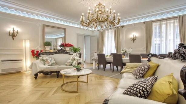 Een ruime woonkamer met een kroonluchter, een eethoek en een zithoek.