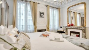 Een hotelkamer met een groot bed, een open haard, een spiegel en een raam met gordijnen.
