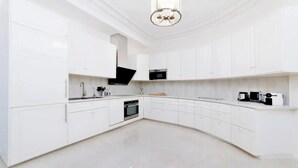 Een moderne keuken met witte kasten, een ingebouwde oven, een magnetron en een koffiezetapparaat.