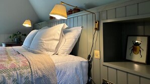 A bedroom with a bed, two bedside lamps, a wall-mounted shelf with a framed picture, and a potted plant. - Hootananny  (Inverness)