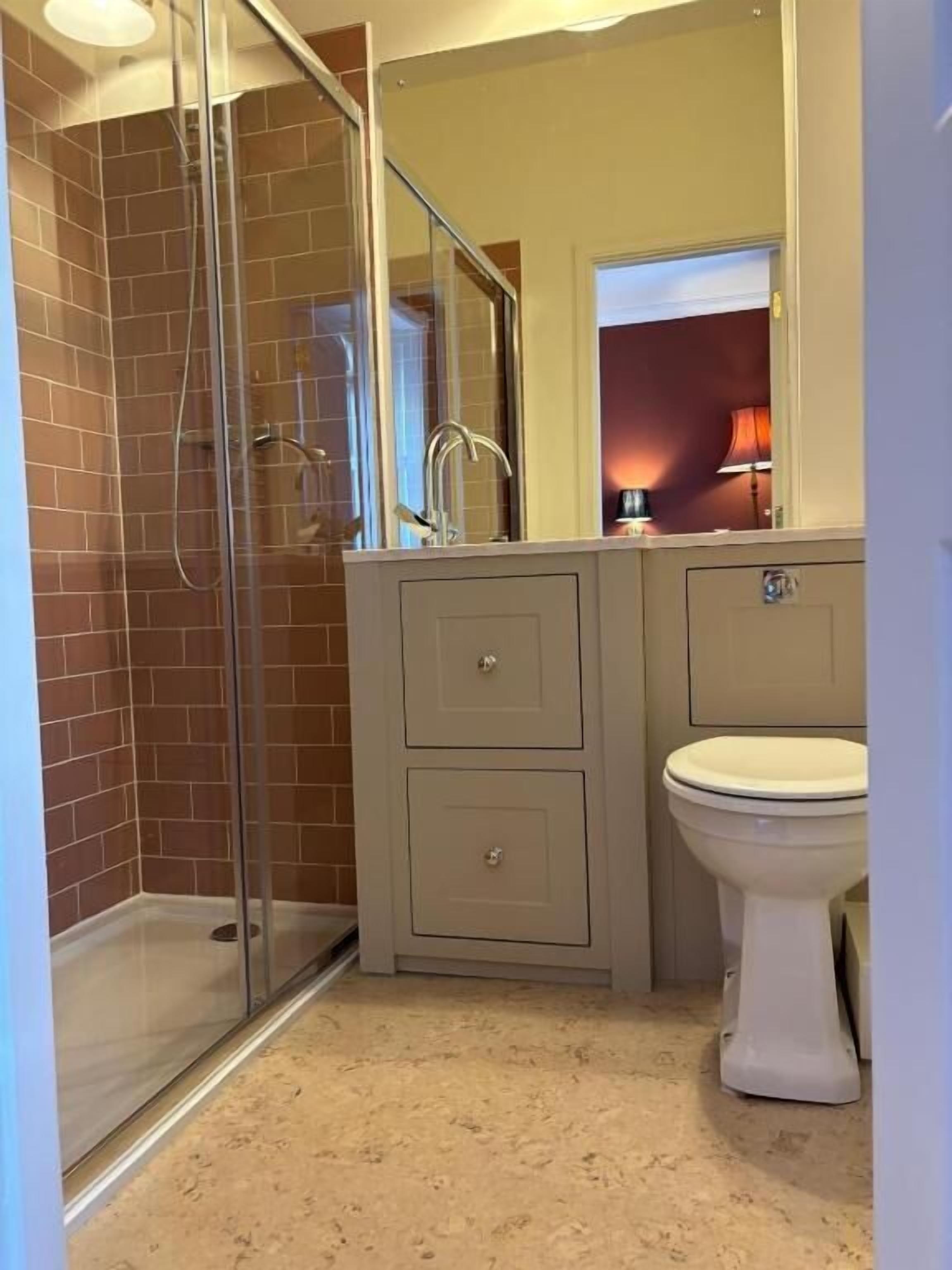 A bathroom with a glass-enclosed shower, a sink with a mirror above it, and a toilet.