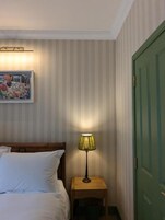 Una habitación de hotel con una cama, una lámpara en una mesita de noche, un cuadro en la pared y una puerta verde.