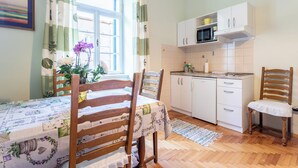 Eine Küche mit weißen Schränken, einer Mikrowelle und einem Spülbecken. Ein Esstisch mit Stühlen und eine Blumenvase sind ebenfalls vorhanden.