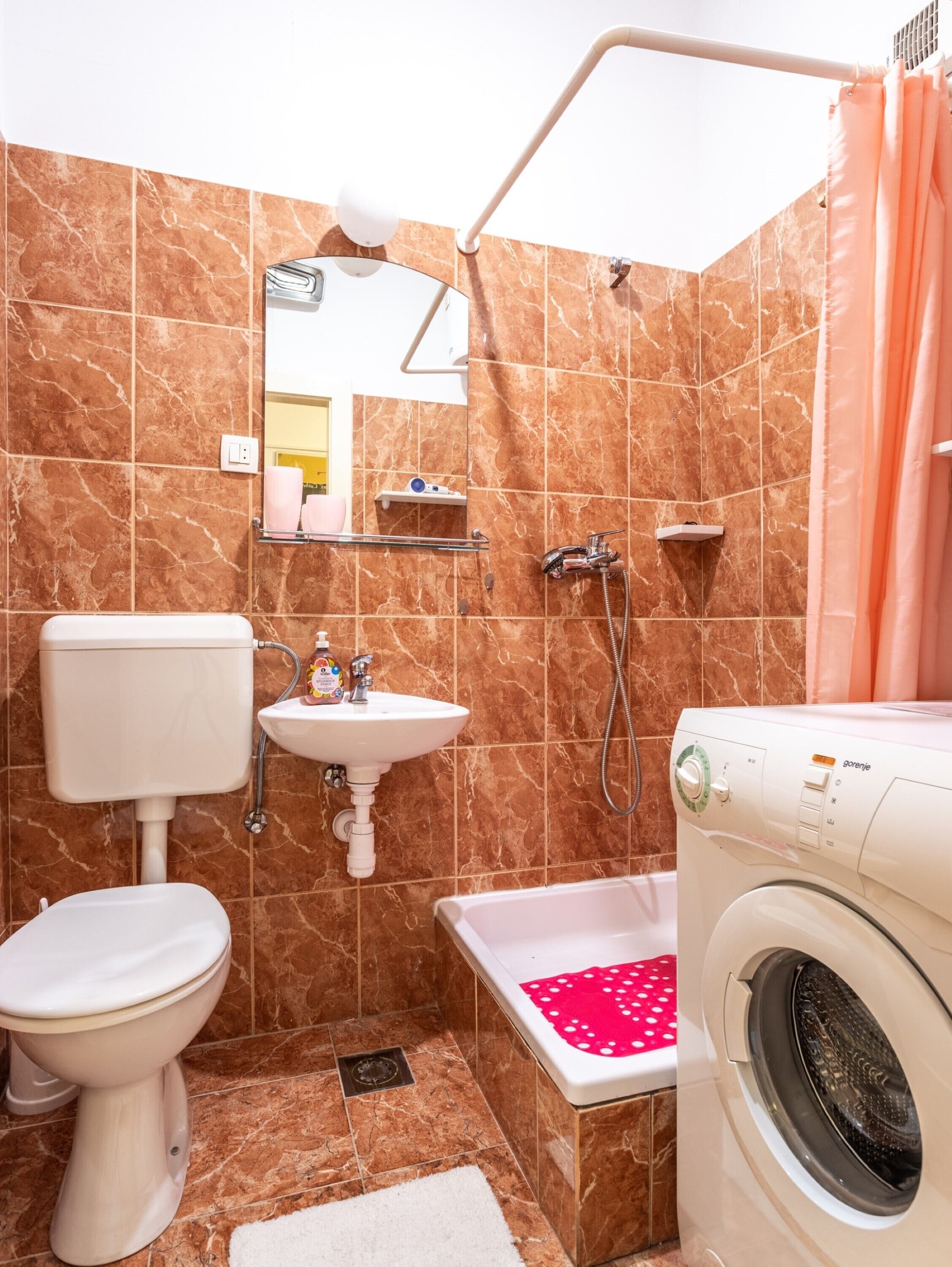 A bathroom with a toilet, sink, shower, and washing machine.