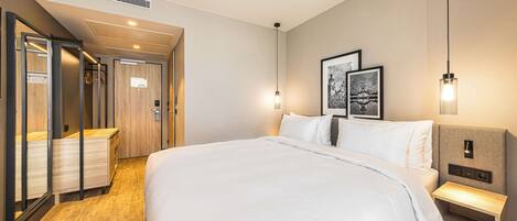 A modern hotel room with a large bed, bedside tables, a wardrobe, and a mirror.
