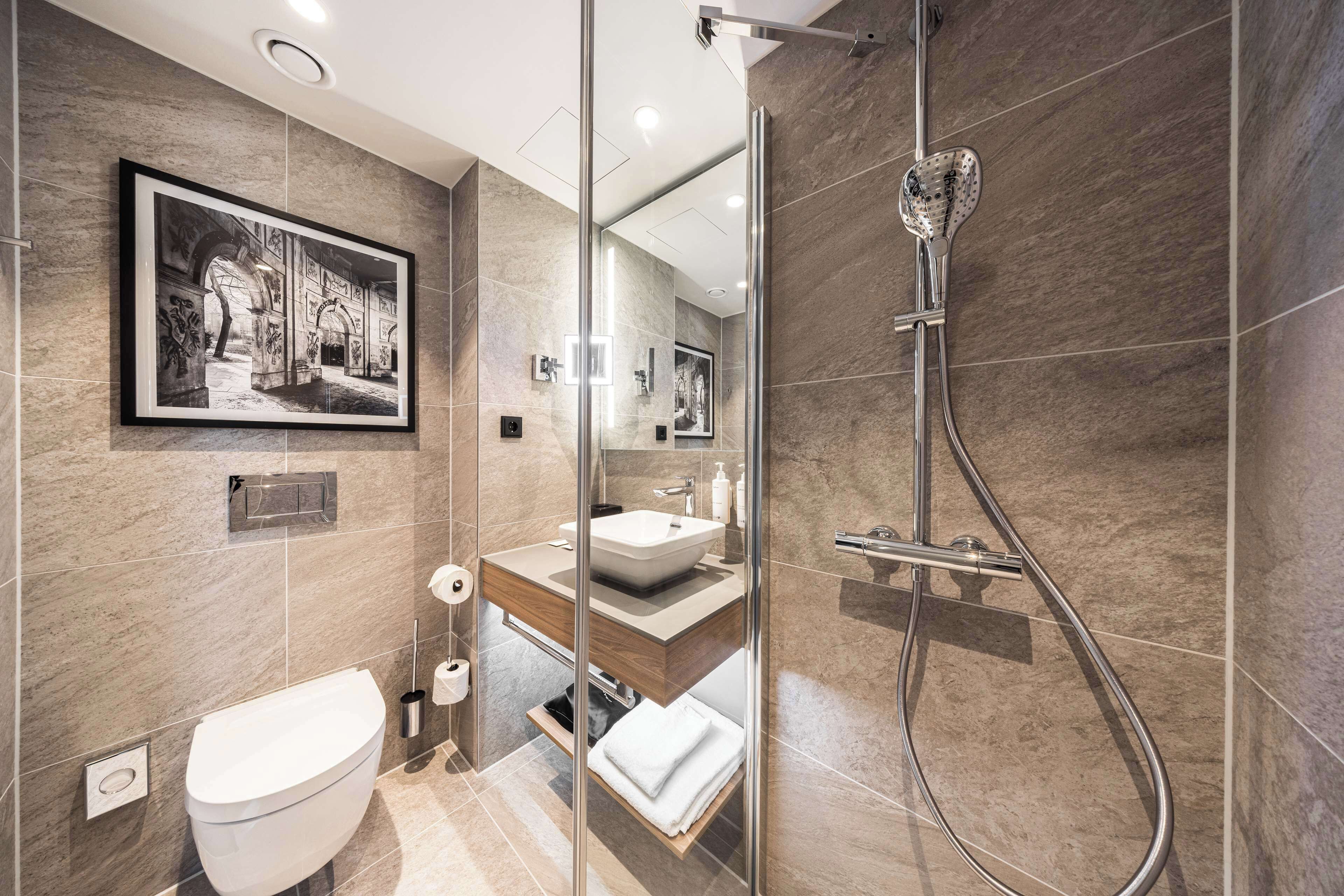 A modern bathroom with a glass-enclosed shower, a sink with a mirror above it, and a framed picture on the wall.