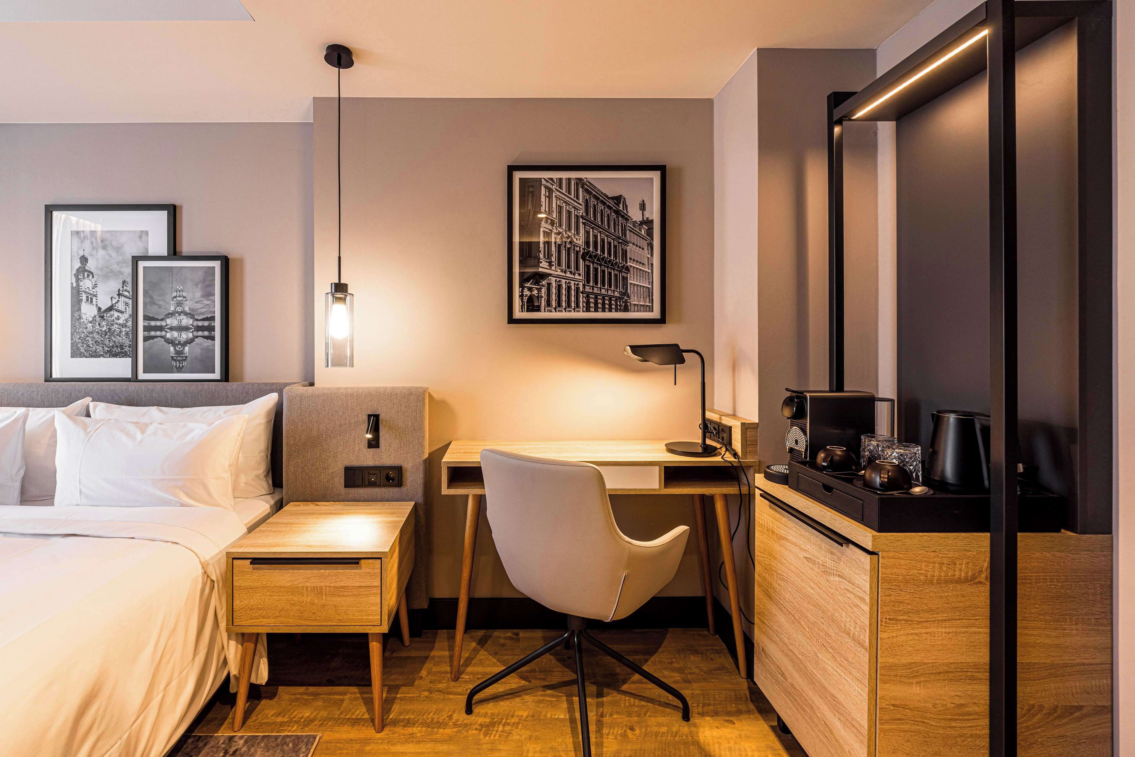 Una camera d'albergo con un letto, una scrivania, una sedia, una macchina per il caffè e quadri appesi alla parete.