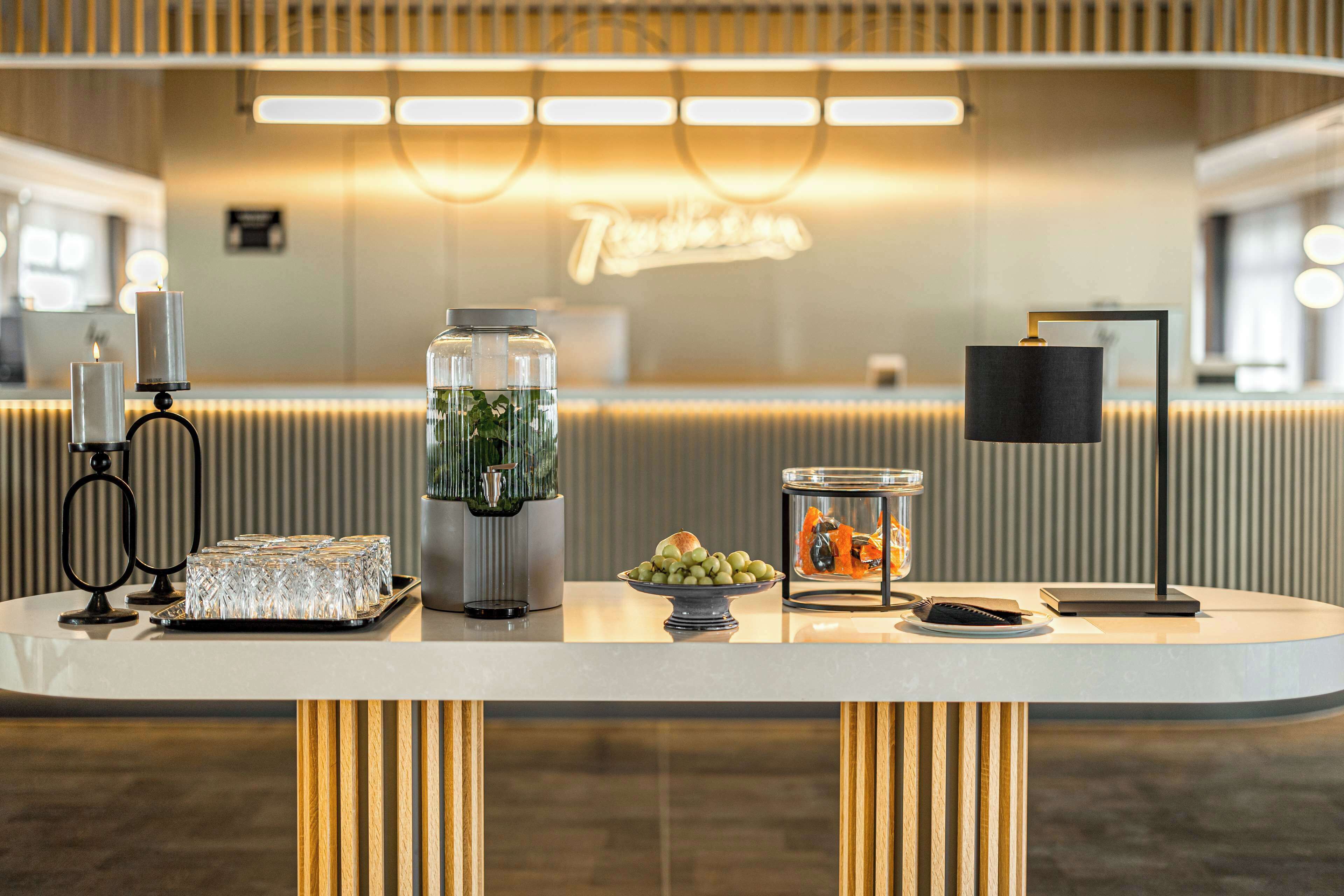 Modernilla designilla sisustettu vastaanottoalue, jossa on vastaanottotiski, lasivitriini, kahvilanurkkaus ja koristeellinen kasvi.