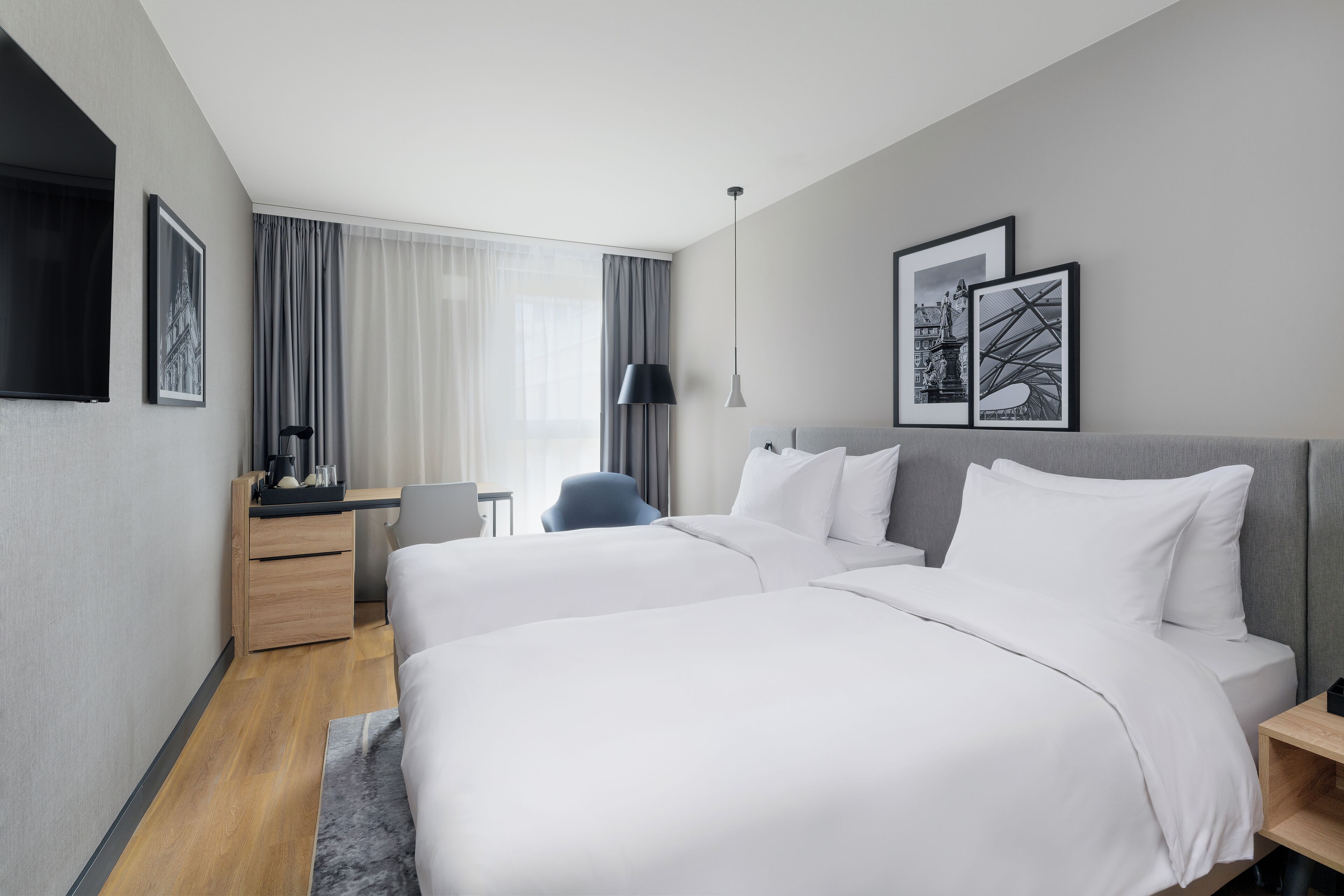 Una habitación de hotel moderna con dos camas, un escritorio, una silla y un ventanal con cortinas.