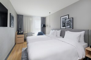 A modern hotel room with two beds, a desk, a chair, and a large window with curtains.