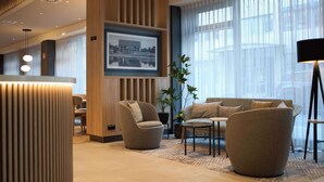 Un vestíbul d'hotel modern amb taulell de recepció, zona de seients i grans finestres.